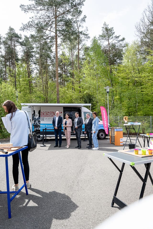 Ihmisiä puiden ympäröimän ulkoilmatietobussin edessä