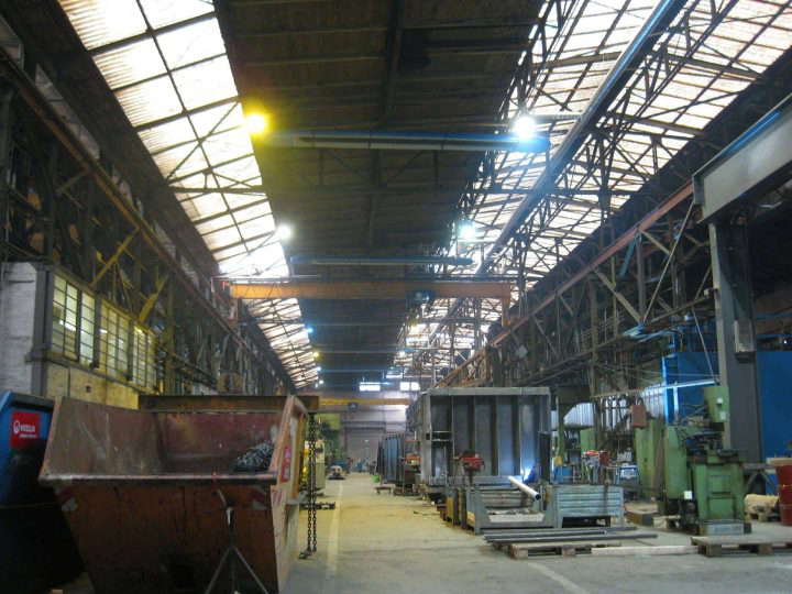 Düstere Produktionshalle mit Containern. Blaue OPTIMA plus Deckenstrahler von KÜBLER werden von den Lampen in Szene gesetzt.