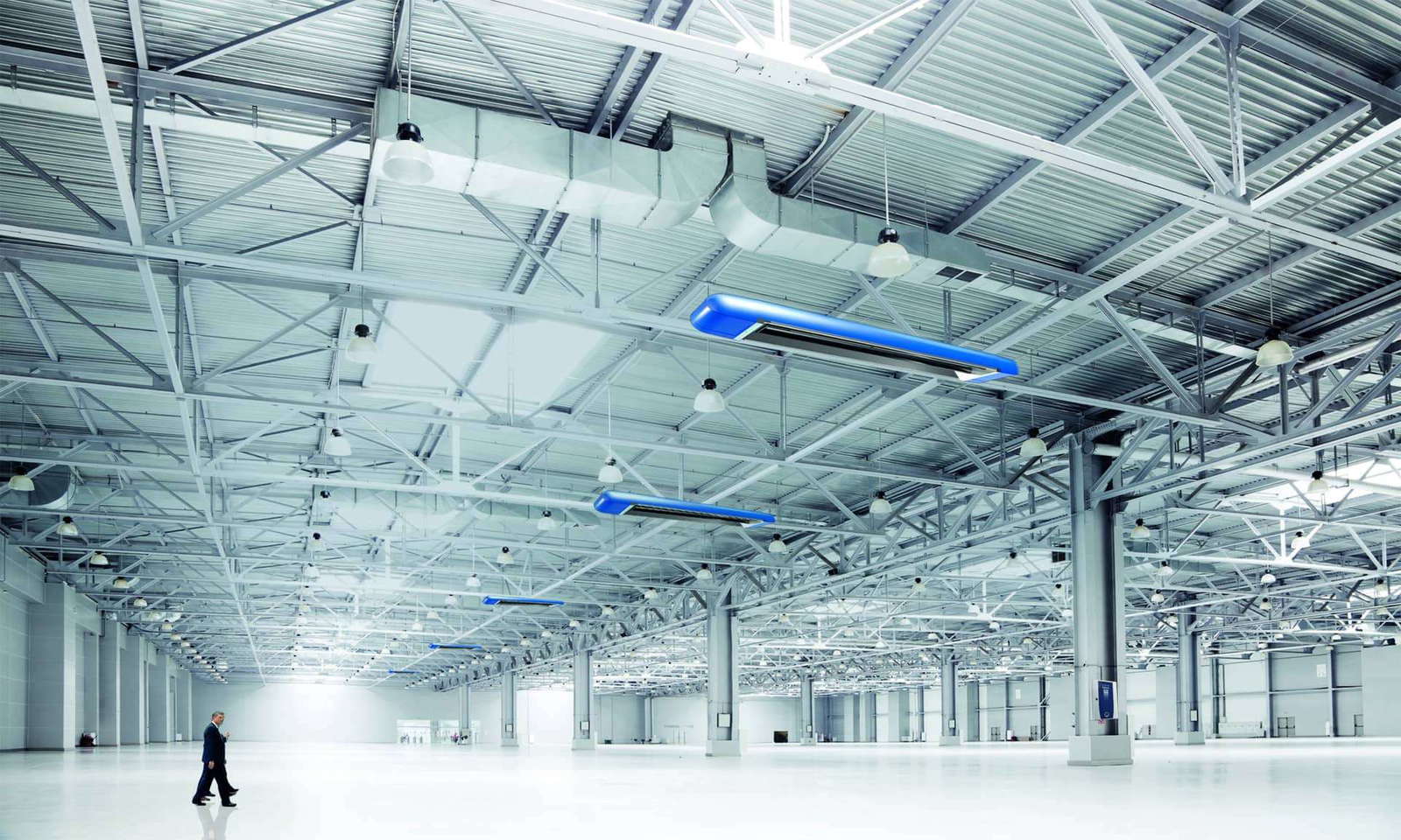 Ein Mann geht alleine durch eine große Industriehalle mit Dunkelstrahlern