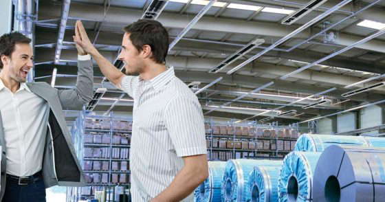 To gründere slår hverandre i hendene med et lykkelig uttrykk i ansiktet. I bakgrunnen skimtes en lagerbygning med PRIMA takspotlights fra KÜBLER.