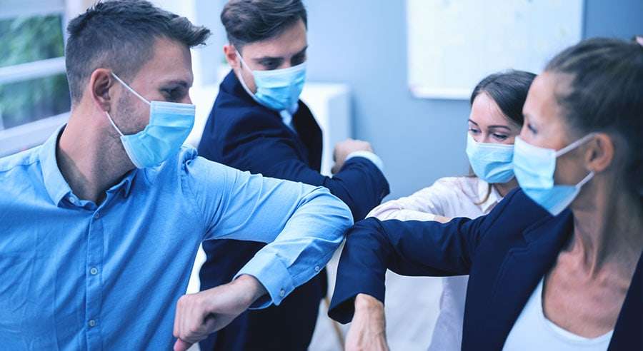 Naamioituneet työntekijät tervehtivät toisiaan kyynärpäällä.