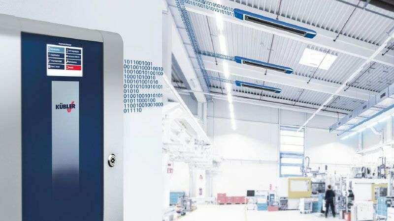 CELESTRA-ohjausjärjestelmä KÜBLERin hallien lämmitysjärjestelmistä, taustalla korjaamo, jossa on sininen OPTIMA plus -hallien lämmitysjärjestelmä, jota CELESTRA ohjaa tarpeen mukaan.