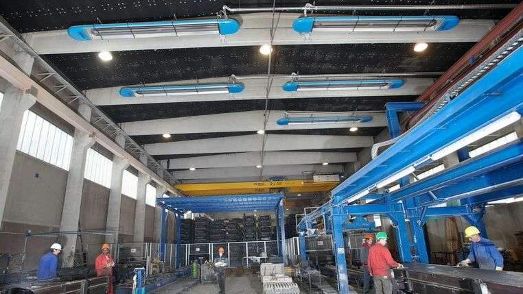 Anwendungsbeispiel von KÜBLERs Hallenheizungssystemen im Produktionsbereich, mit Arbeitern, die optimal während der Arbeit aufgewärmt werden