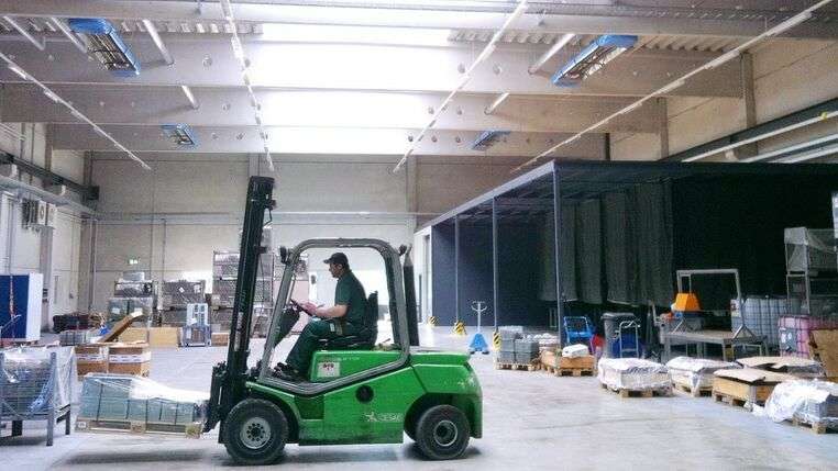 Logistikhalle im Vordergrund ist ein Gabelstaplerfahrer zu sehen. Die halle ist ausgerüstet mit OPTIMA plus Infrarotheizungen von KÜBLER