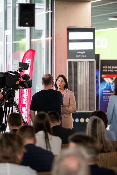 Woman being interviewed, audience in the background.