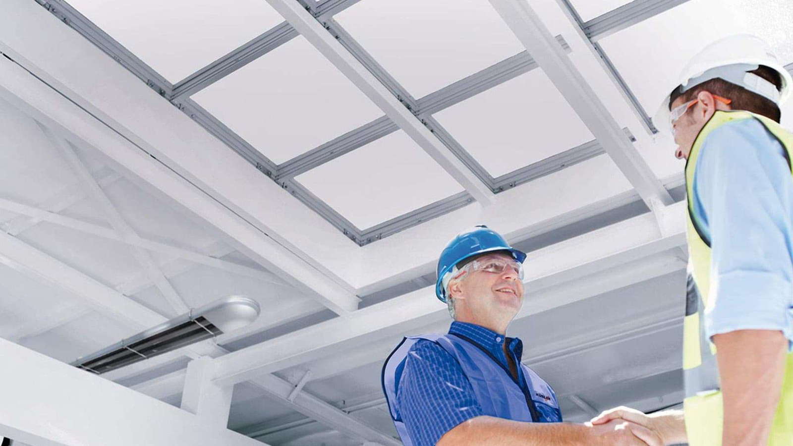 Arbeiter in einer Halle schütteln sich zufrieden die Hände, im Hintergrund ist ein Deckenstrahler von KÜBLER Hallenheizungen angebracht
