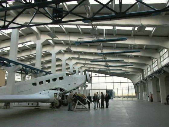 Flugzeughalle mit historischem Flugzeug und Besuchern.