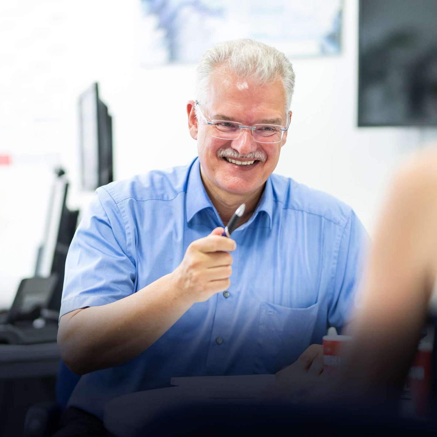 Hymyilevä mies toimistossa kynän kanssa.