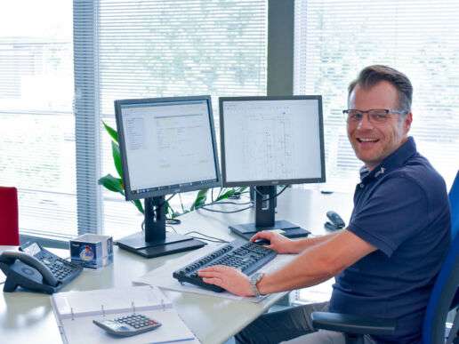 Ein Mitarbeiter der Firma KÜBLER sitzt lachend vor zwei Monitoren und ist gerade dabei, ein Projekt abzuarbeiten.