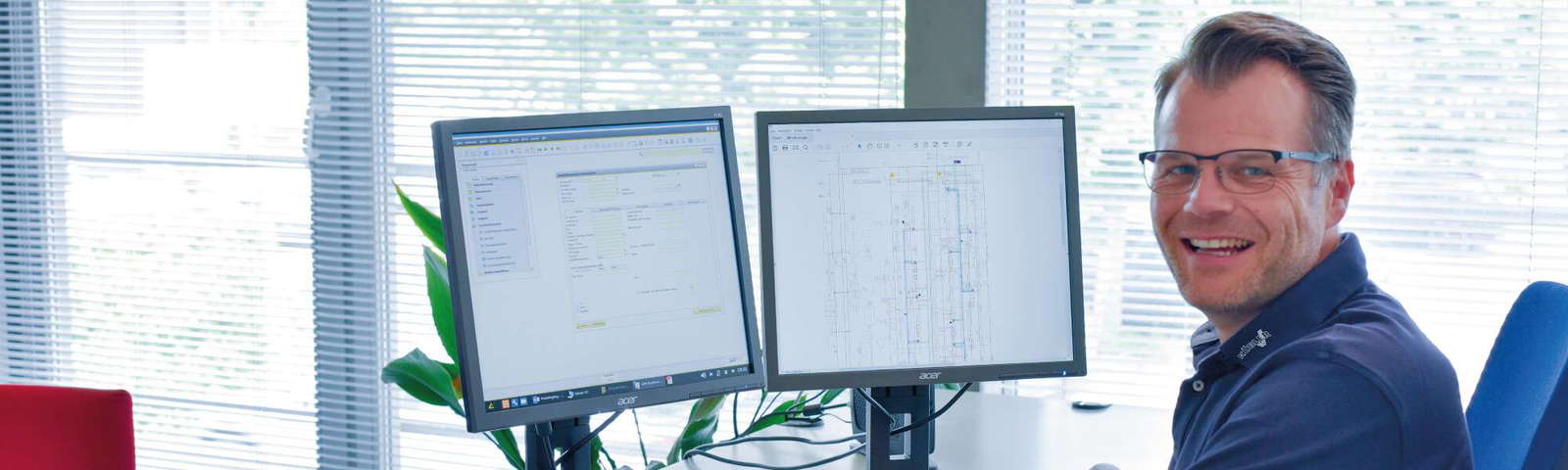 Ein Mitarbeiter der Firma KÜBLER sitzt lachend vor zwei Monitoren und ist gerade dabei, ein Projekt abzuarbeiten.