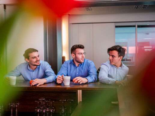 Drei Männer beim Gespräch am Tisch.