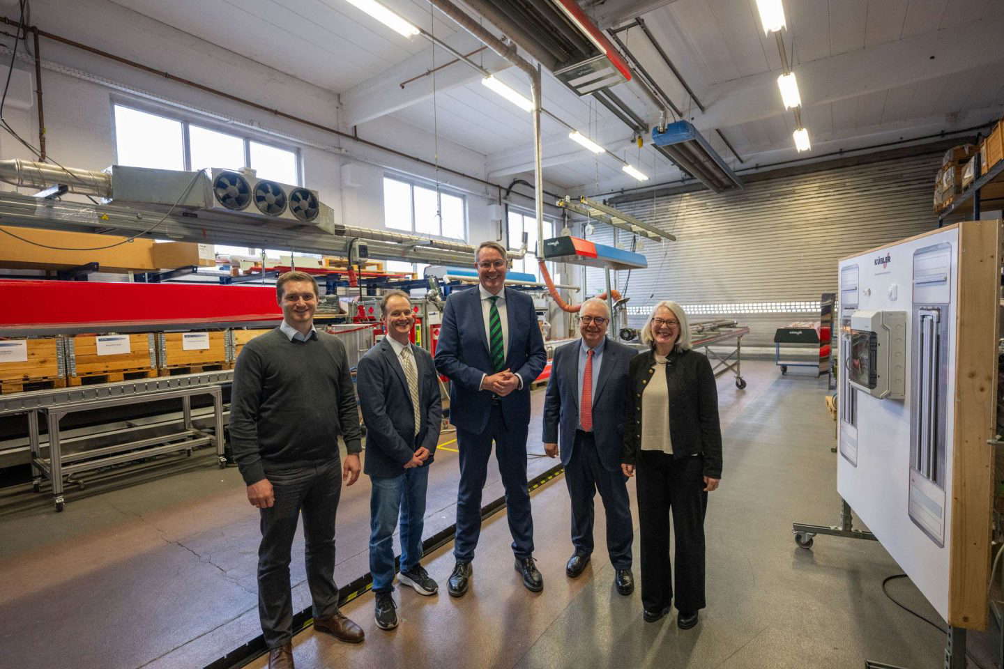 Fünf Personen lächeln in einer Industriehalle