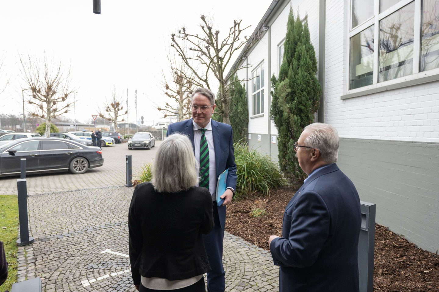 Drei Personen treffen sich vor einem Gebäude