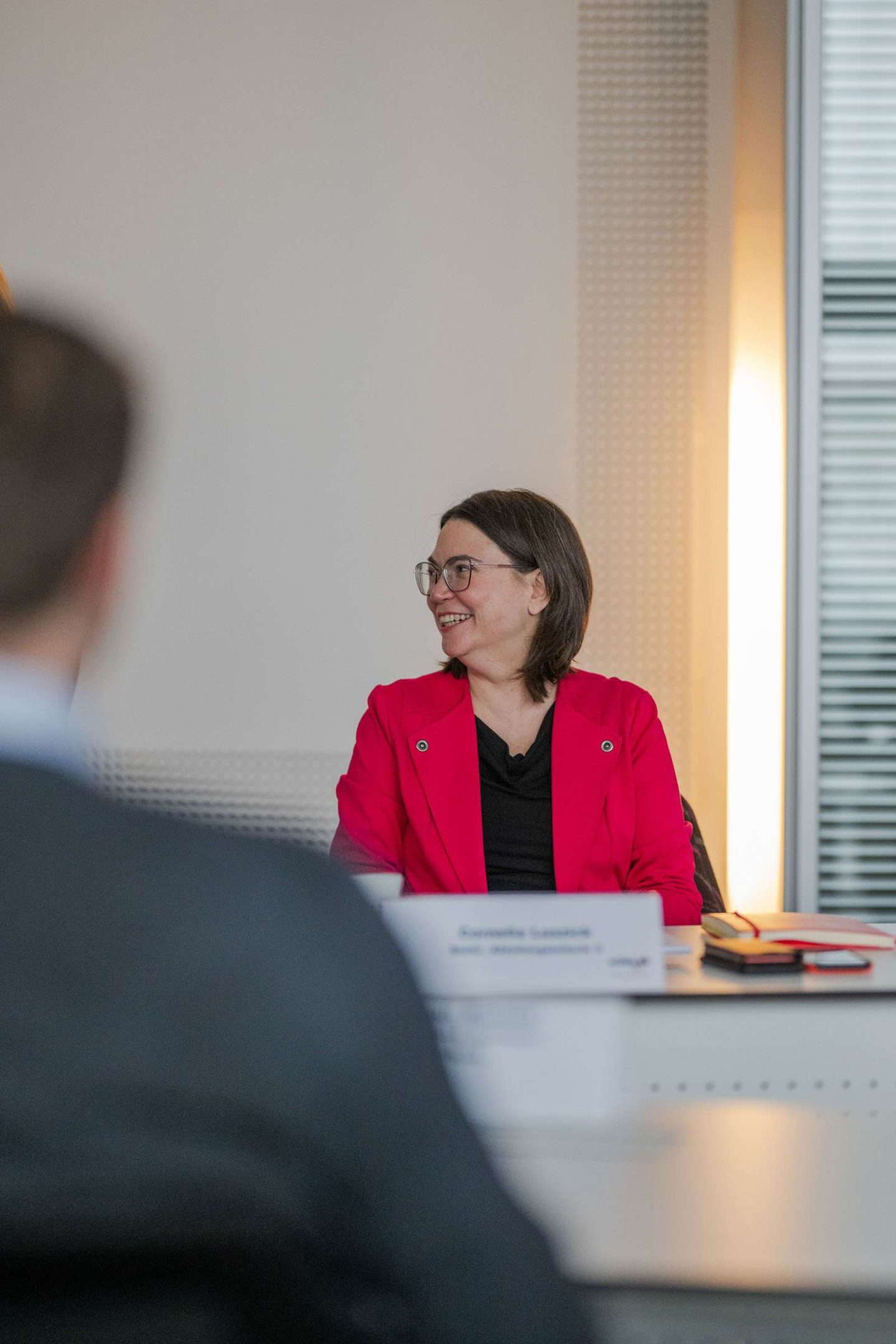 Frau in rotem Blazer lächelt während Besprechung