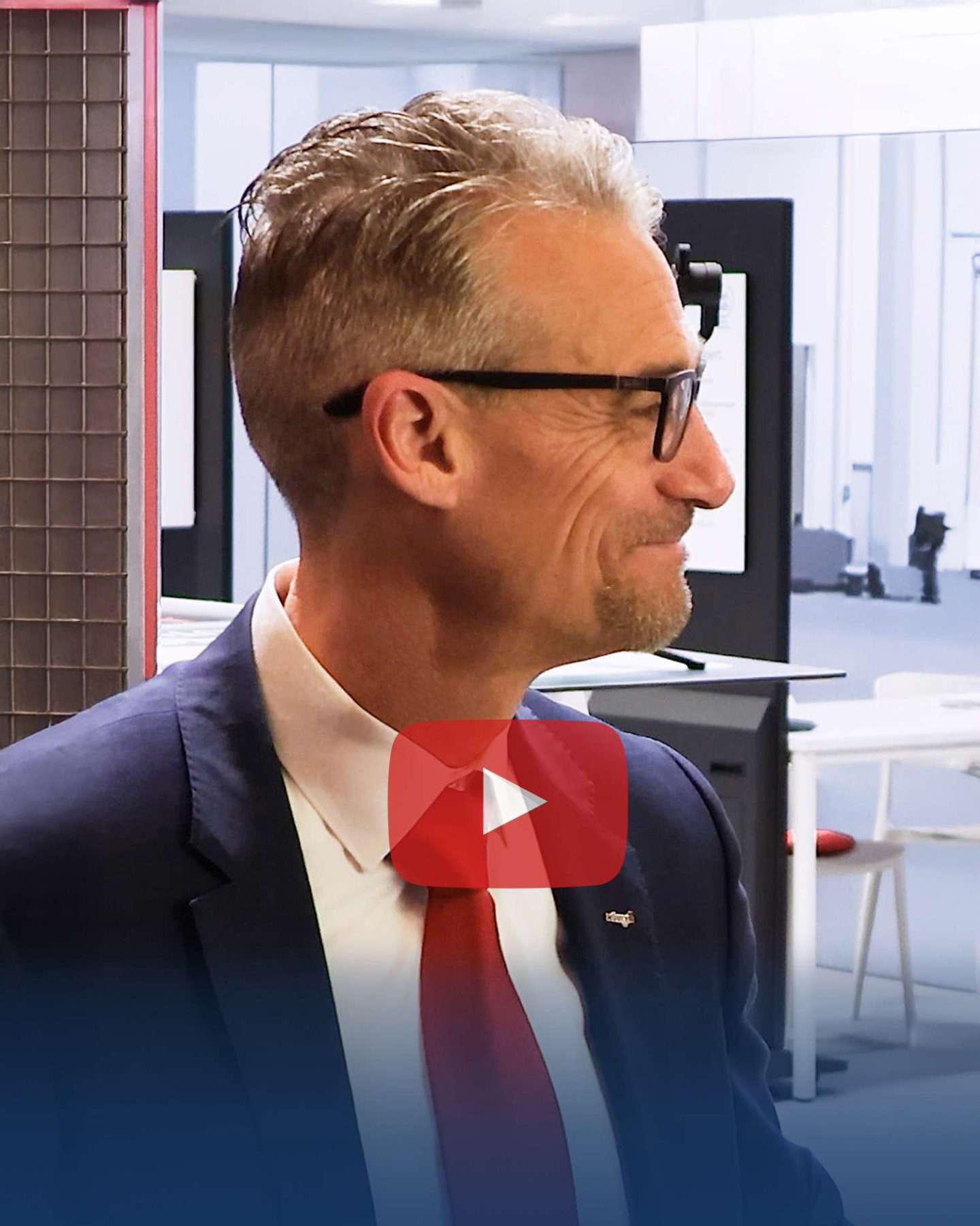 Mann med briller smiler på et moderne kontor