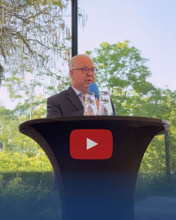 Mies pitää puhetta korokkeella, jossa on YouTube-logo