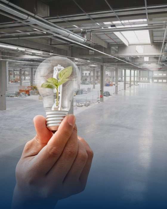 Hand hält Glühbirne mit Pflanze in Fabrikhalle